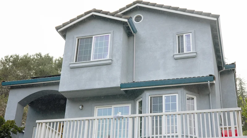 A two-story gray house with a balcony, featuring large windows and a tiled roof.