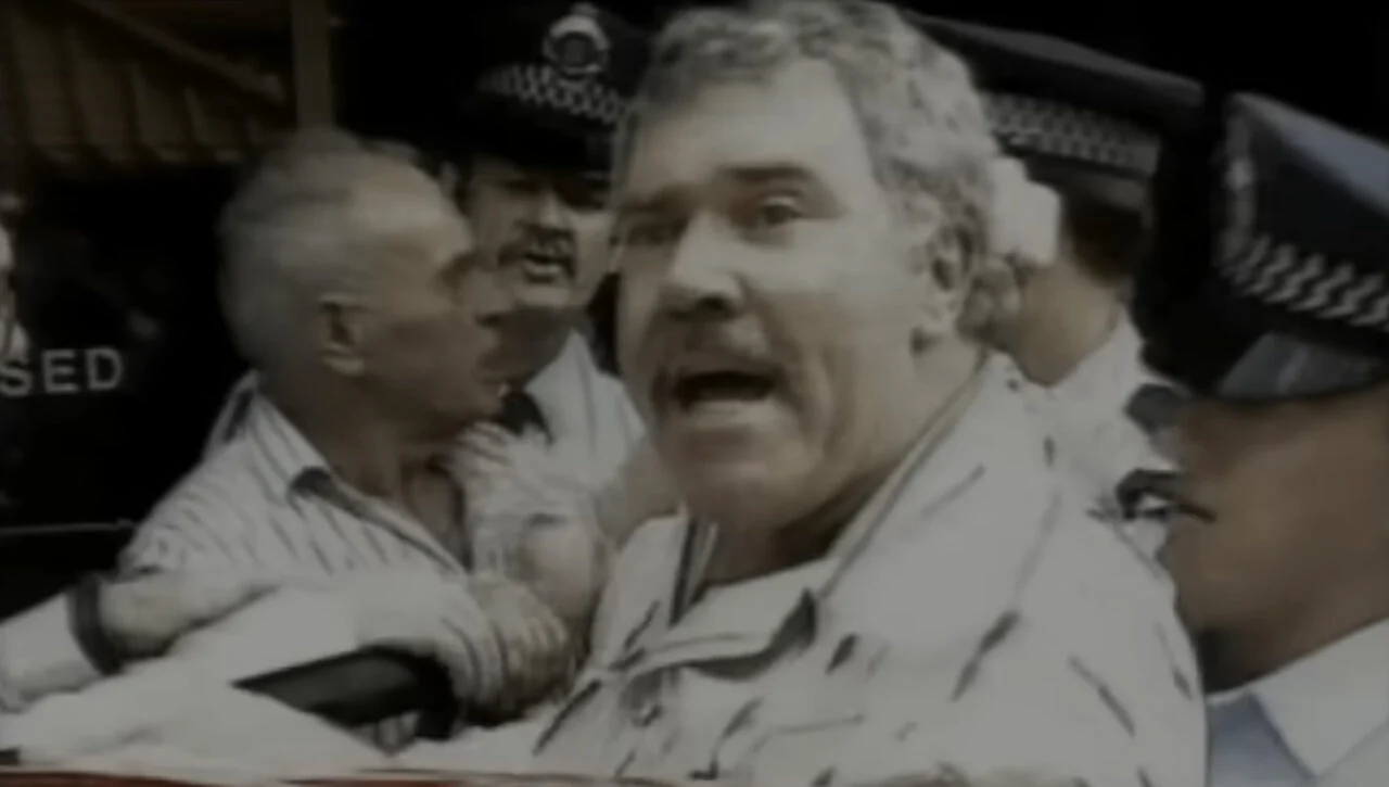 Still image of Jack Karlson being forced into a police car while shouting.