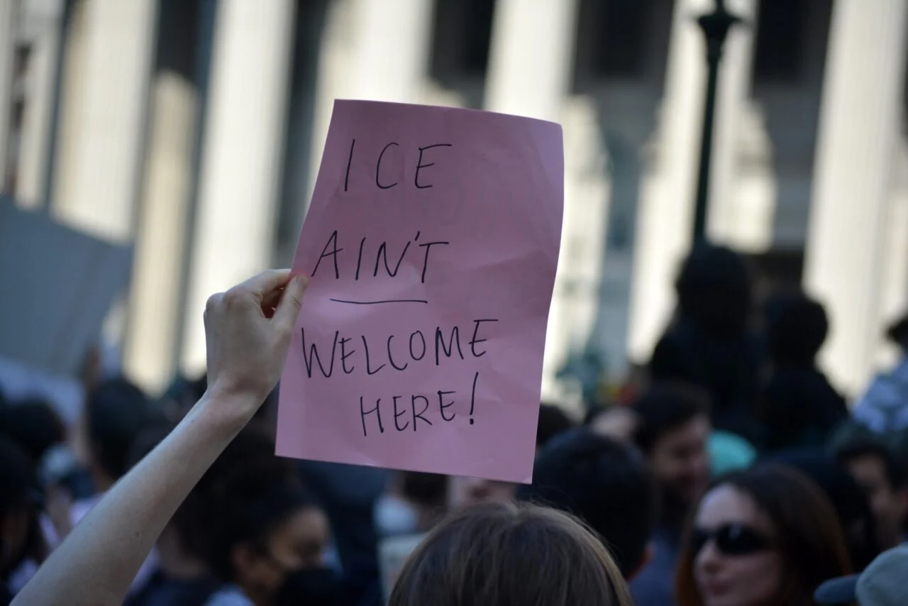A pink sign at an anti-ICE protest in New York taht reads "ICE ain't welcome here!"