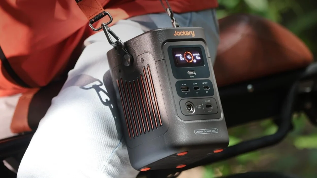 the Jackery Explorer 240D slung over a sholder and sitting on a person's leg while they ride a bicycle