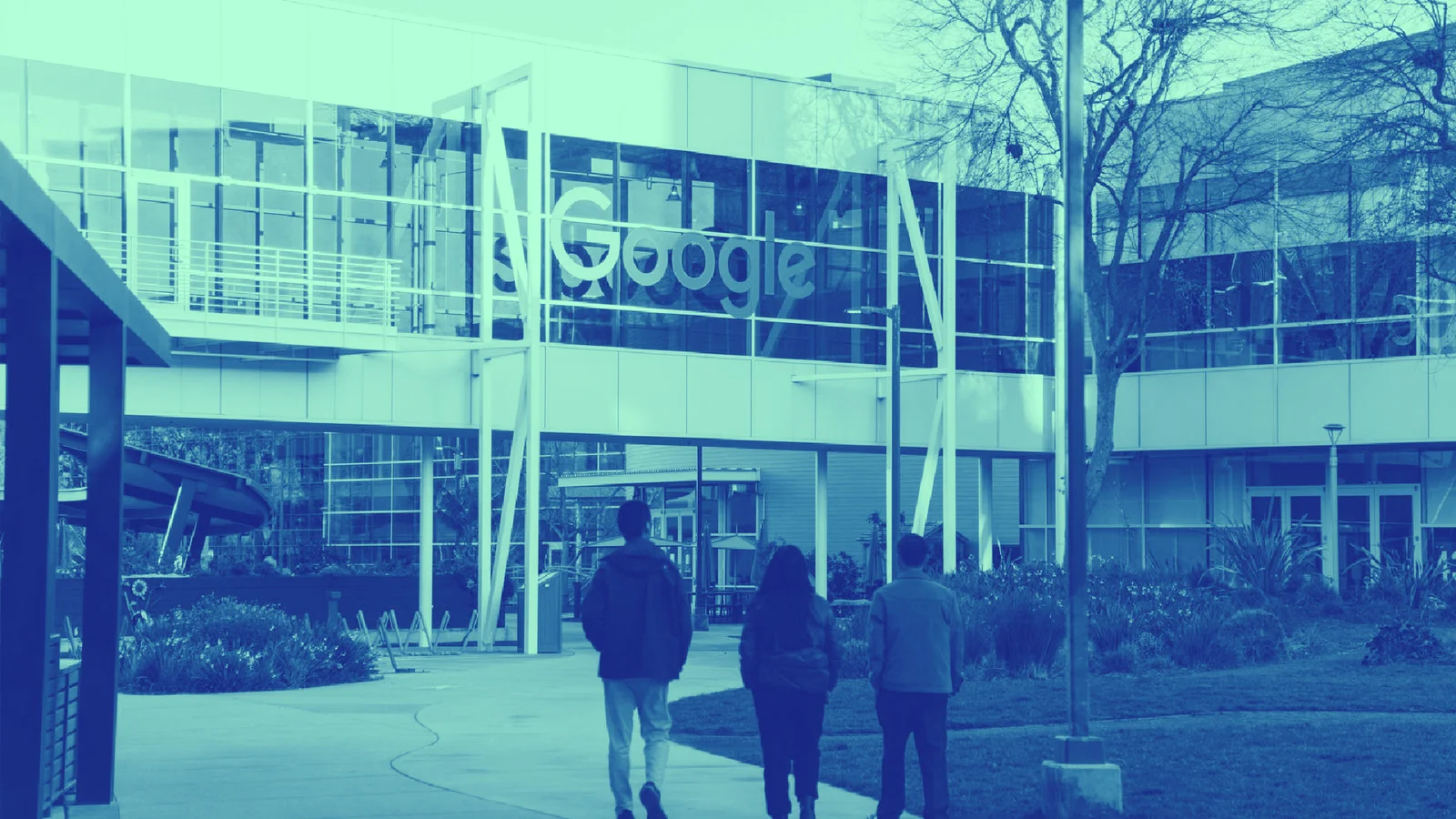 Four people walk towards a modern Google building with large glass windows and a prominent logo.