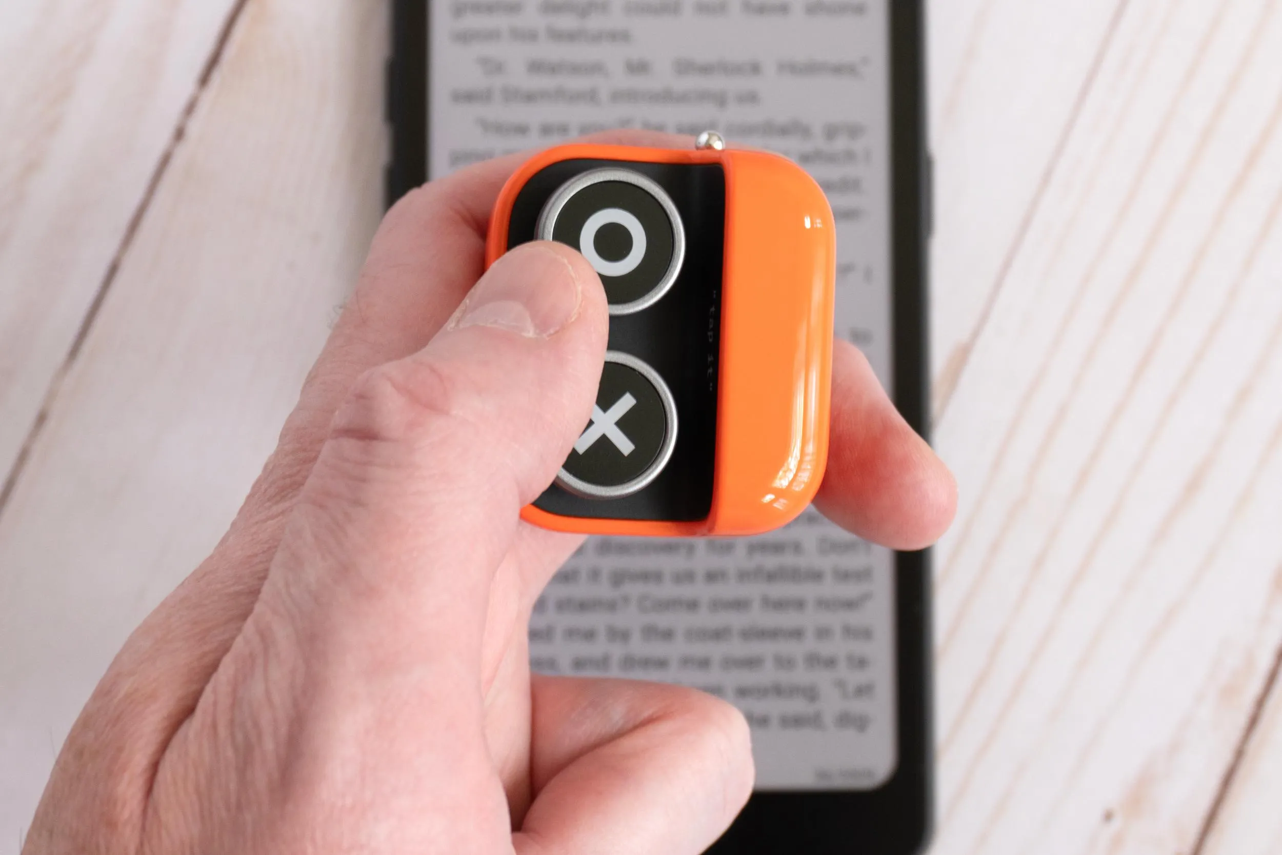 A person holding and pressing a button on the Boox Tappy with an e-reader in the background.
