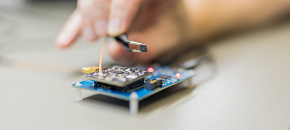 Qualinx QLX3xx chip held in tweezers above a circuit board