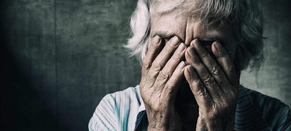 Close-up of an older woman with gray hair covering her face with both hands.