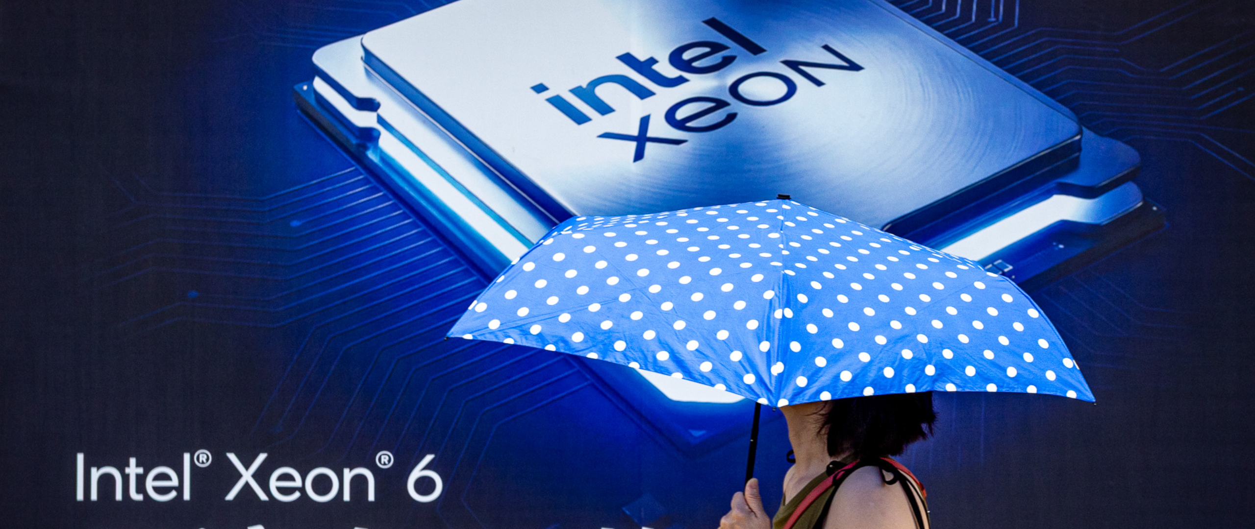 A pedestrian holding a blue polka-dot umbrella walks past a large Intel Xeon 6 processor advertisement during preparation for COMPUTEX 