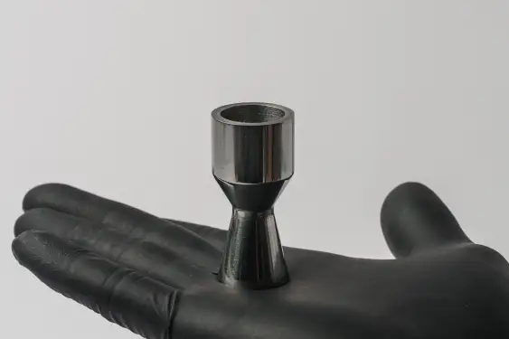 A gloved hand holds a metal part shaped like a rocket nozzle.