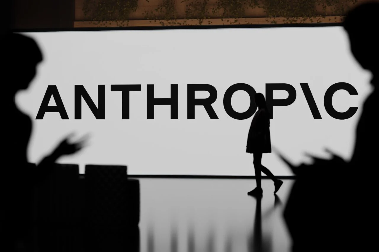 Silhouetted figures in front of a large sign showing the Anthropic logo.