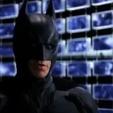 Batman stands in front of computer screens.