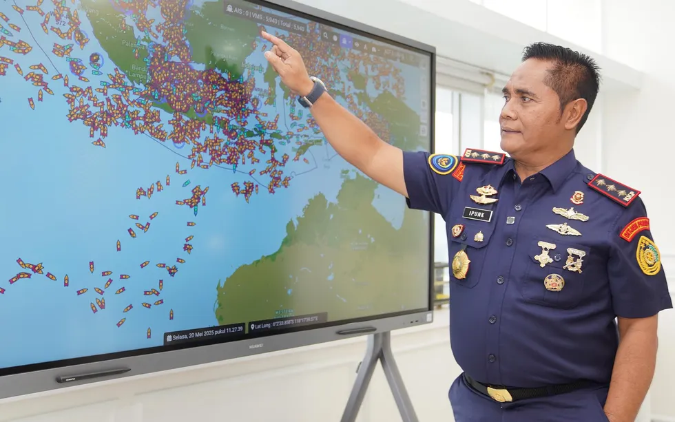 A man in an Indonesian military uniform points to a large monitor showing an overview of thousands of fishing boats at sea near Indonesia.